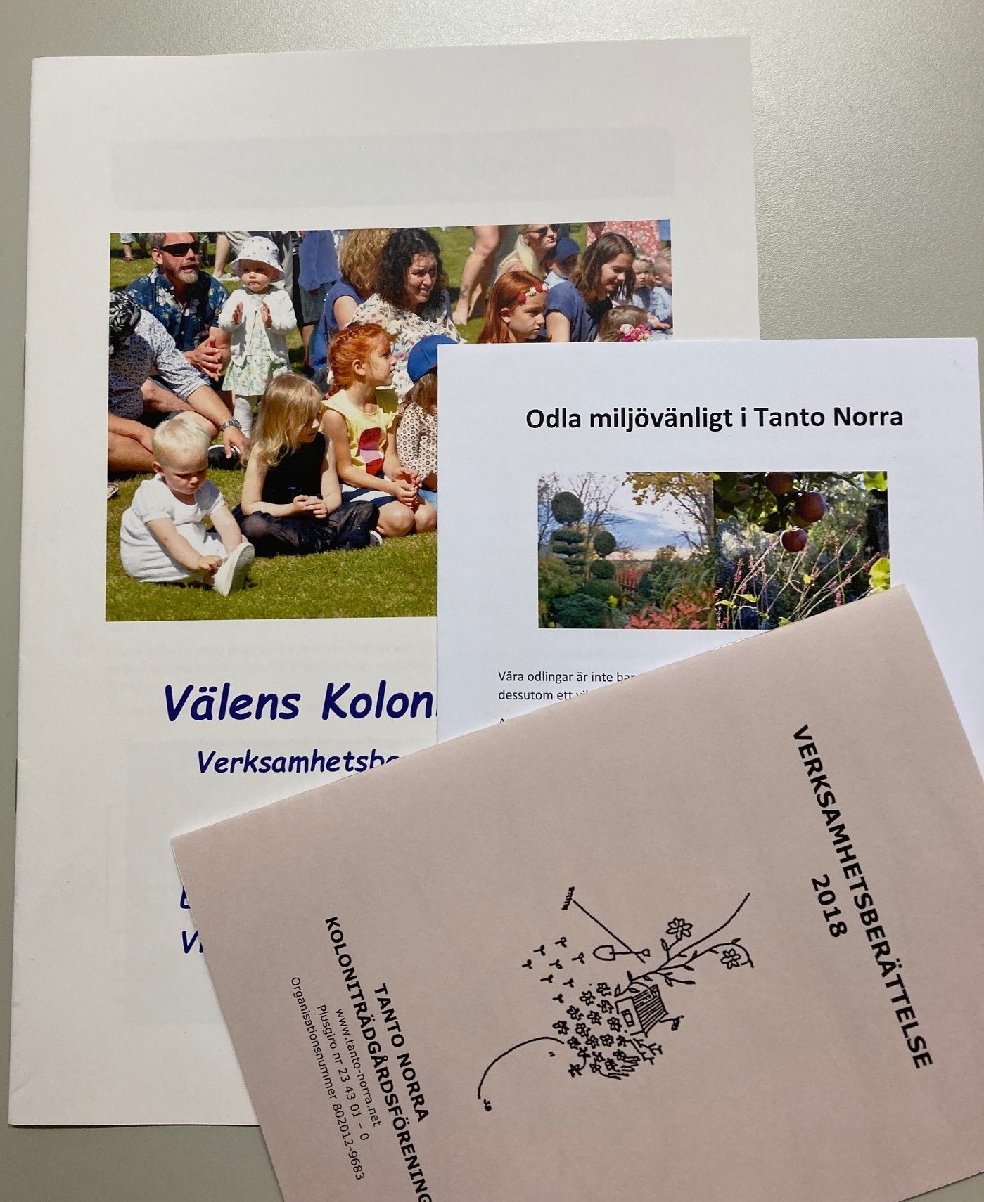 Färgfoto av tre trycksaker med omslagsbilder som visar barnfamiljer och trädgårdsmiljöer