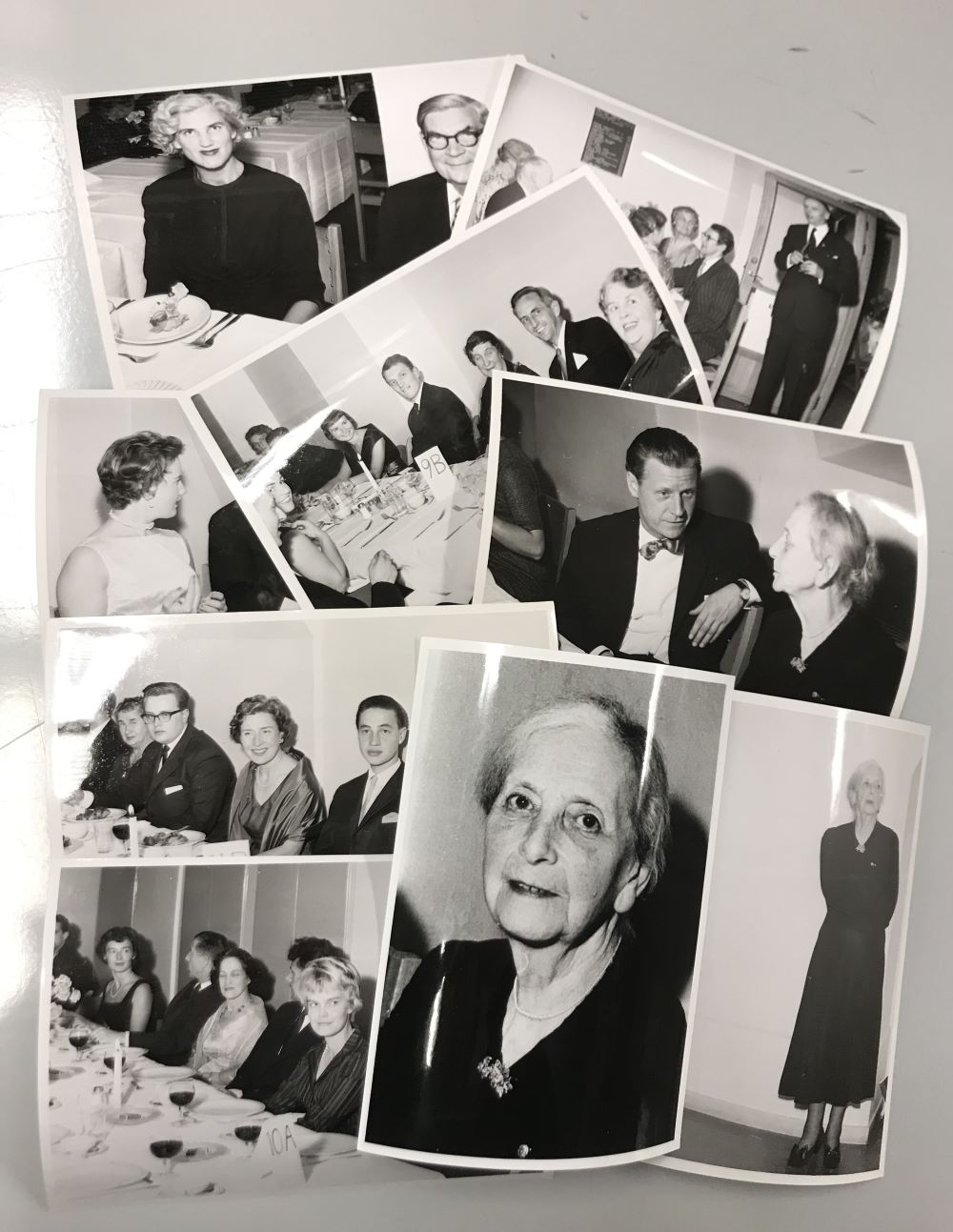 Nio utspridda svartvita fotografier med festklädda människor som delvis syns sittande vid middagsbord. Ett foto föreställer en ensam äldre kvinna i svart klänning. På ett annat foto syns hennes ansikte i närbild.