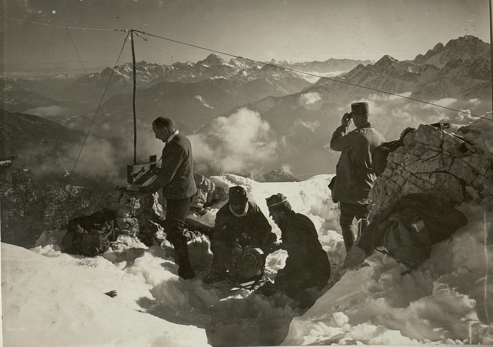 Fyra män sitter på en snöig bergstopp och skickar ut radiosignaler. Svartvitt foto.