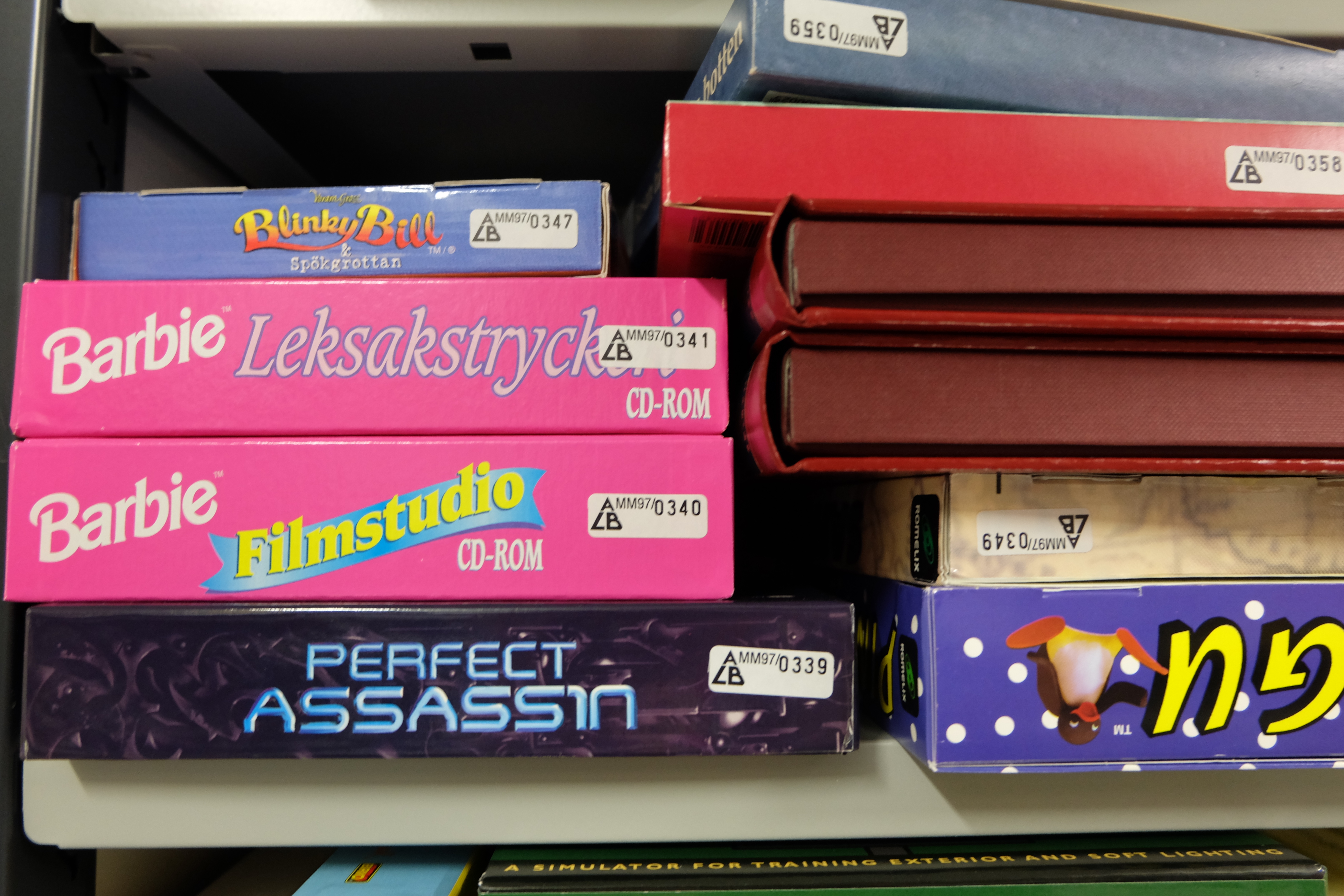 Shelf with computer games. At the front are some pink covers with the text "Barbie".